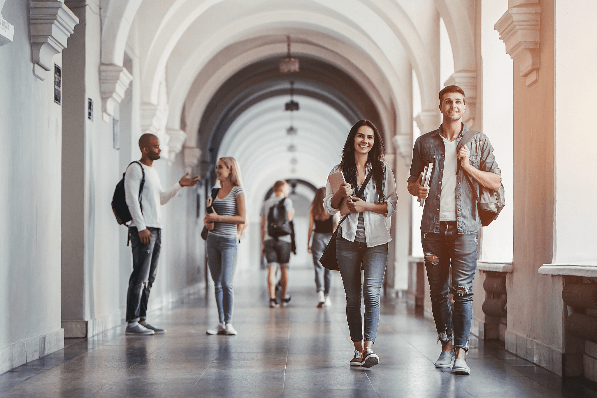 Six personnes qui semblent être des étudiants marchent dans des corridors avec des sacs à dos ou des sacs en bandoulières. Photo.